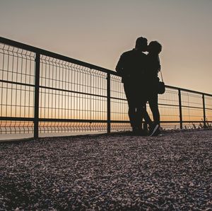 Rear view of silhouette people standing on railing against sky during sunset