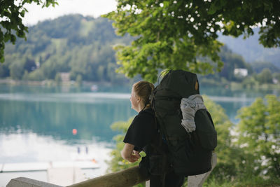 Rear view of woman standing by lake against trees