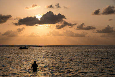 Silhouette people on sea against sky during sunset