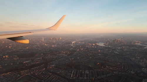 Cropped image of aircraft wing flying against sky over cityscape