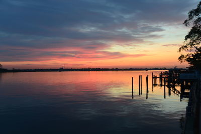 Silhouette wooden post in river against sky during sunset