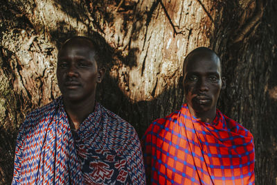 Two masai men in traditional clothes standing under big mkungu tree