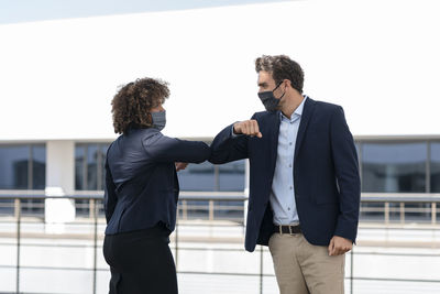 Colleagues giving elbow bump while greeting at office building terrace