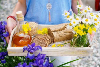 Close-up of young woman offering breakfast tray with flower bouquet