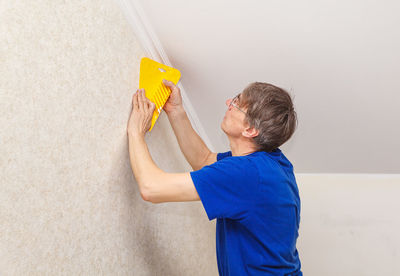 Mature painter using scrapper on wall