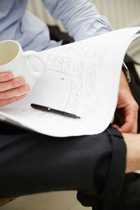Cropped image of businessman with blueprints having coffee at creative office