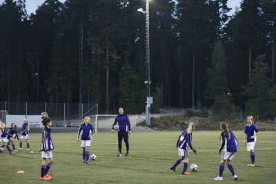 Coach looking at girls playing soccer on field