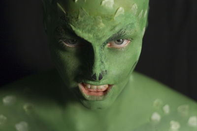 Close-up portrait of man with green body paint in darkroom