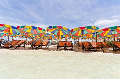 Colorful beach umbrellas by deck chairs on sand against sky