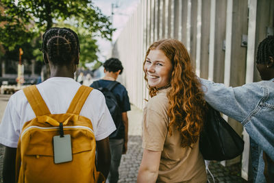 Portrait of happy teenage girl looking over shoulder while walking with friends in city