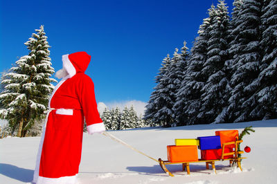Side view of santa claus pulling sled with colorful gifts on snow during winter