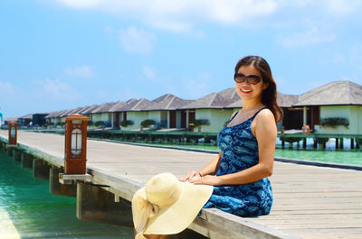 Portrait of smiling woman sitting on pier over sea