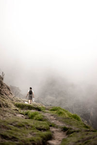 Rear view of woman walking on mountain during foggy weather