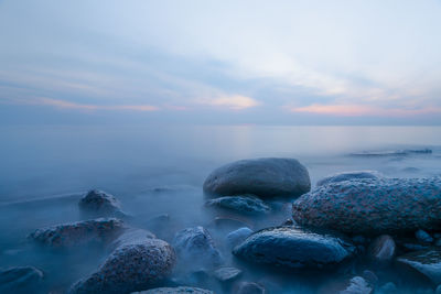 Rocks in sea against sky during sunset