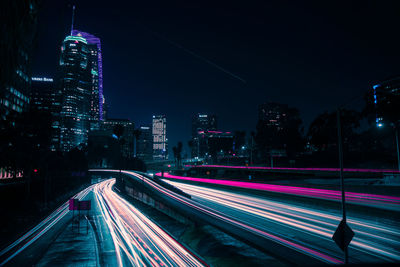 Light trails on street amidst illuminated buildings in city at night