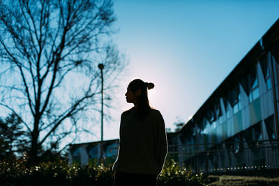 Silhouette woman standing in city against sky during sunset