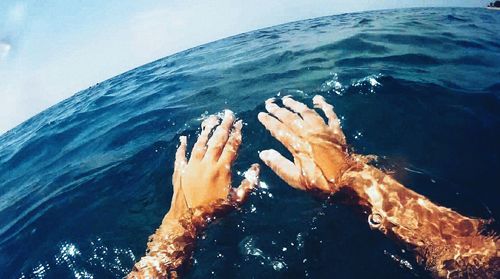 Close-up of hand by sea against blue sky