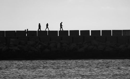 Silhouette people on pier over sea against clear sky