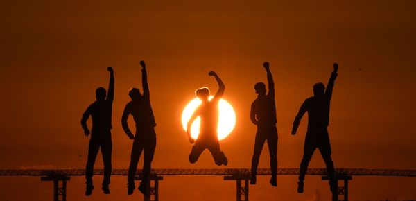 Silhouette people on beach against sky during sunset