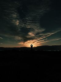 Silhouette man standing on landscape against sunset sky