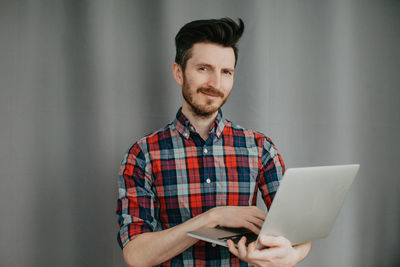 Handsome young man in a plaid shirt by a grey background with laptop. high quality photo