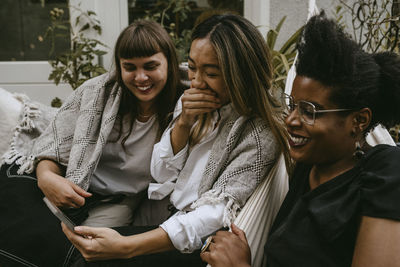 Cheerful friends looking at mobile phone while enjoying during garden party