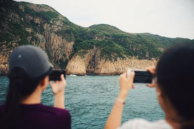 Rear view of people photographing sea against clear sky