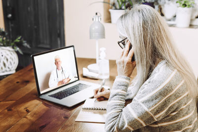 Woman using phone while sitting on table at home