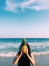 Woman hiding face with pineapple at beach
