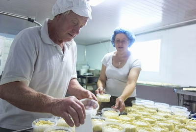 Man packing cheese in box while standing with colleague at dairy