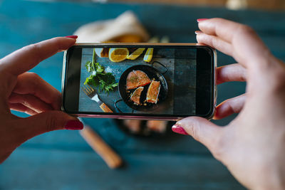 Closeup of hands taking a picture of salmon fillets with parsley and lemon