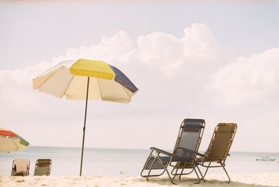 Empty chairs on beach against sky