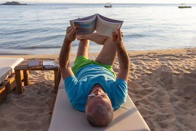 Mature man lying on a sunbed and reading a book at sunset. summer vacation concept.