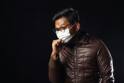 Man in mask coughing while standing against black background