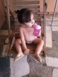 High angle view of shirtless girl drinking water while sitting on swing