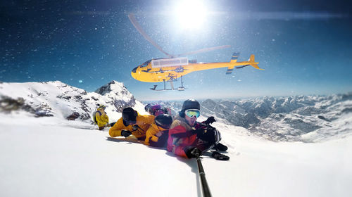 People snowboarding on snowcapped mountain against helicopter flying in sky