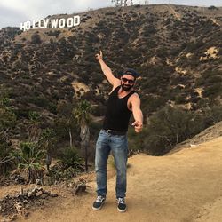 Portrait of smiling man gesturing towards hollywood sign on mountain