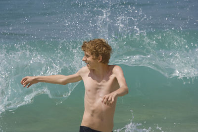 Shirtless teenage boy against wave splashing in sea