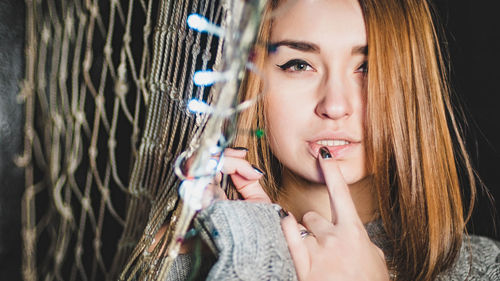 Portrait of beautiful woman with finger on lips standing by illuminated netting