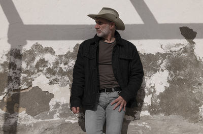 Portrait of adult man in cowboy hat and jeans against wall with sunlight and shadow. almeria, spain