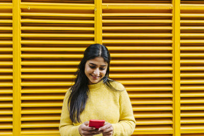 Woman with mobile phone standing at yellow wall