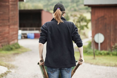 Rear view of female farmer pushing wheelbarrow on rural road