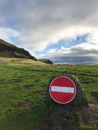Road sign on field against sky
