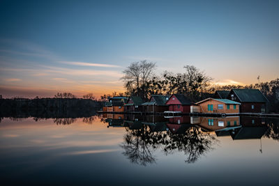 Houses by lake against sky during sunset