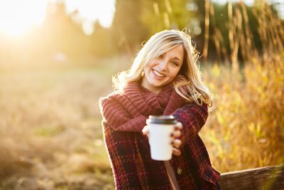 Young woman holding coffee cup while standing on field