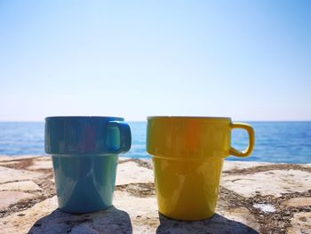Close-up of coffee cup on beach against clear sky