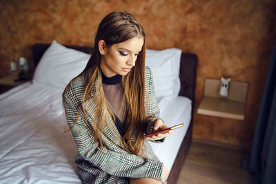 Young woman using phone while sitting on bed at home