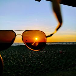 Close-up of sunglasses on beach against sky during sunset