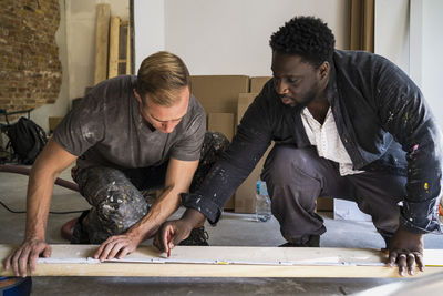 Diverse male carpenters marking with pencil on plank while working in apartment