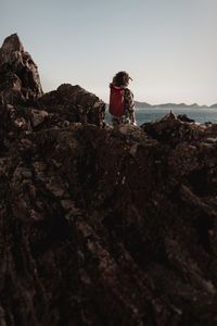 Rear view of woman standing on rock against sky